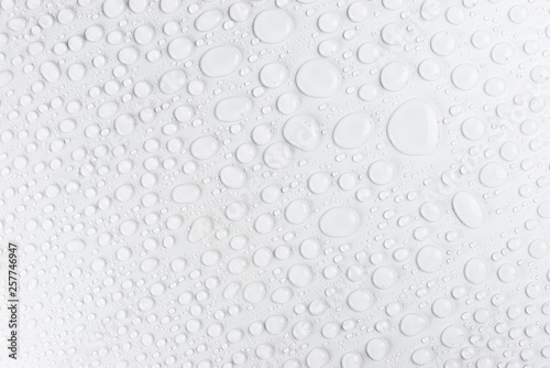 Droplets of water on a white, matte background illuminated with a delicate light.