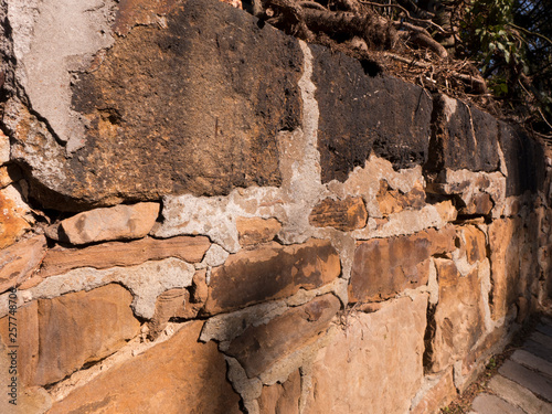 Ein Mauer aus Bruchstein. Einige Fugen sind mit Zement verfugt. Es ist ein sonniger Tag.