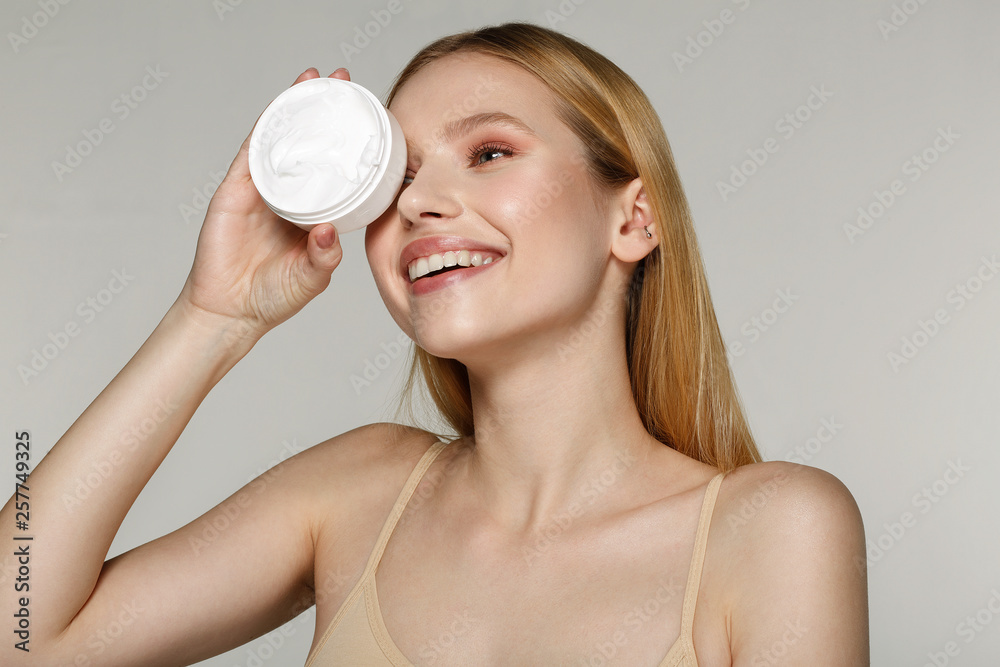 Smiling beautiful half naked woman with blonde hair hide one eyes with cream tube Smiling beautiful half naked woman with blonde hair hide one eyes with cream tube