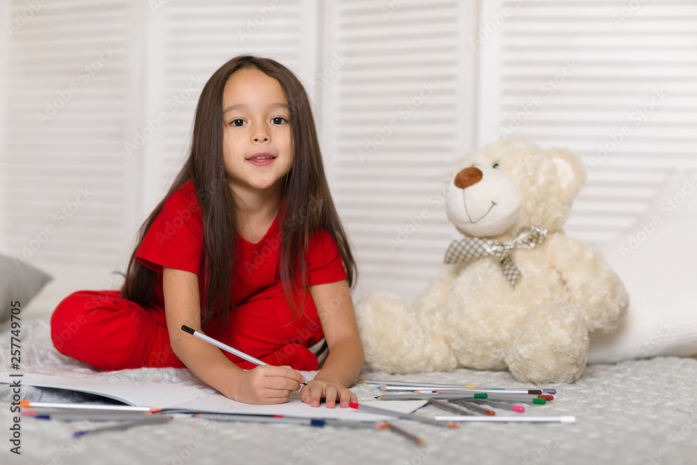 cute little child girl in red pajamas with teddy bear draws with pencils at home cute little child girl in red pajamas with teddy bear draws with pencils at home