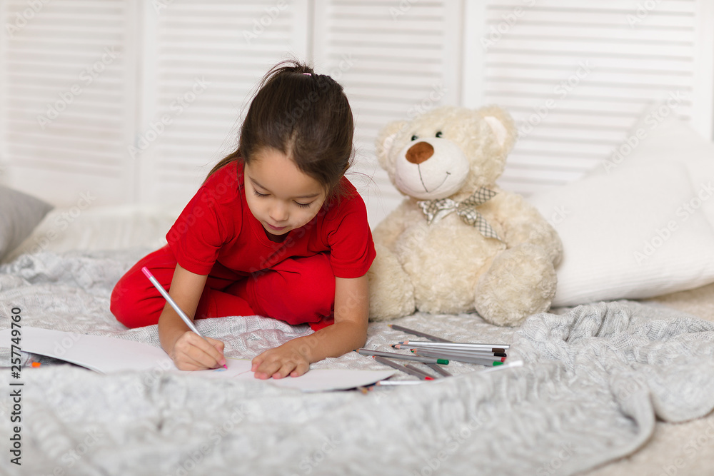 cute little child girl in red pajamas with teddy bear draws with pencils at home cute little child girl in red pajamas with teddy bear draws with pencils at home