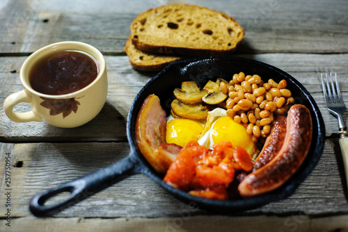 full irish breakfast with fried egg, sausages, black pudding, white pudding, baked beans, bacon, tomato and grilled mushrooms in a cast iron pan