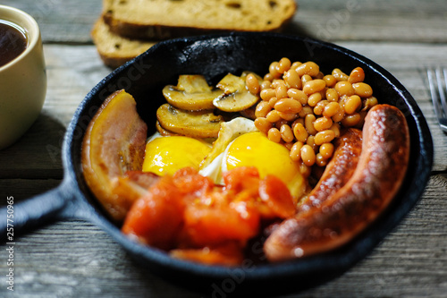 full irish breakfast with fried egg, sausages, black pudding, white pudding, baked beans, bacon, tomato and grilled mushrooms in a cast iron pan