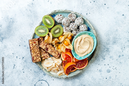 Healthy vegan dessert snacks - protein granola bars, homemade raw energy balls, cashew butter, toasted coconut chips, cape gooseberry, kiwi, blood orange. Concept of healthy sweets for children.