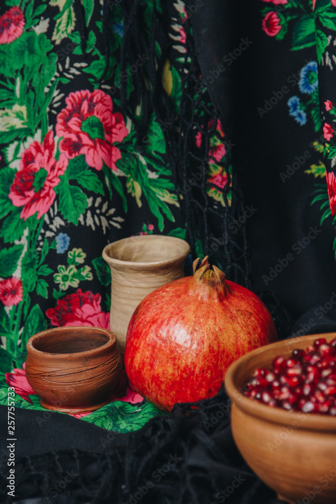 pomegranate grains in a ceramic bowl on a vintage fabric background, pomegranate fruit, ceramic jug, ceramic plate, ethnic shawl, Romma shawl, still life