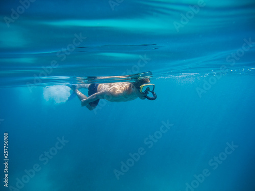 young man swimming and snorkeling with mask and fins in clear blue water