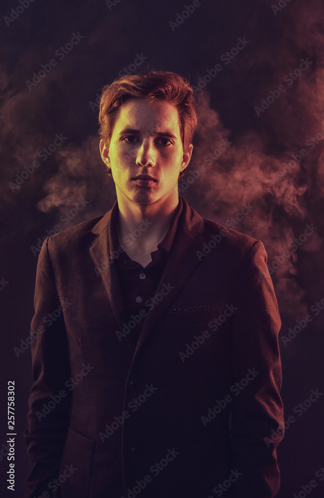 Obraz premium Portrait of an expressive, stylish, young man in a strict suit in orange tones with a smoky background
