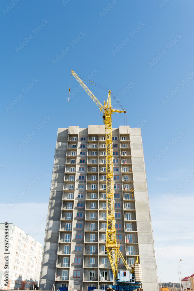 Fototapeta premium yellow tower crane and the construction of a multi-storey building against a blue sky