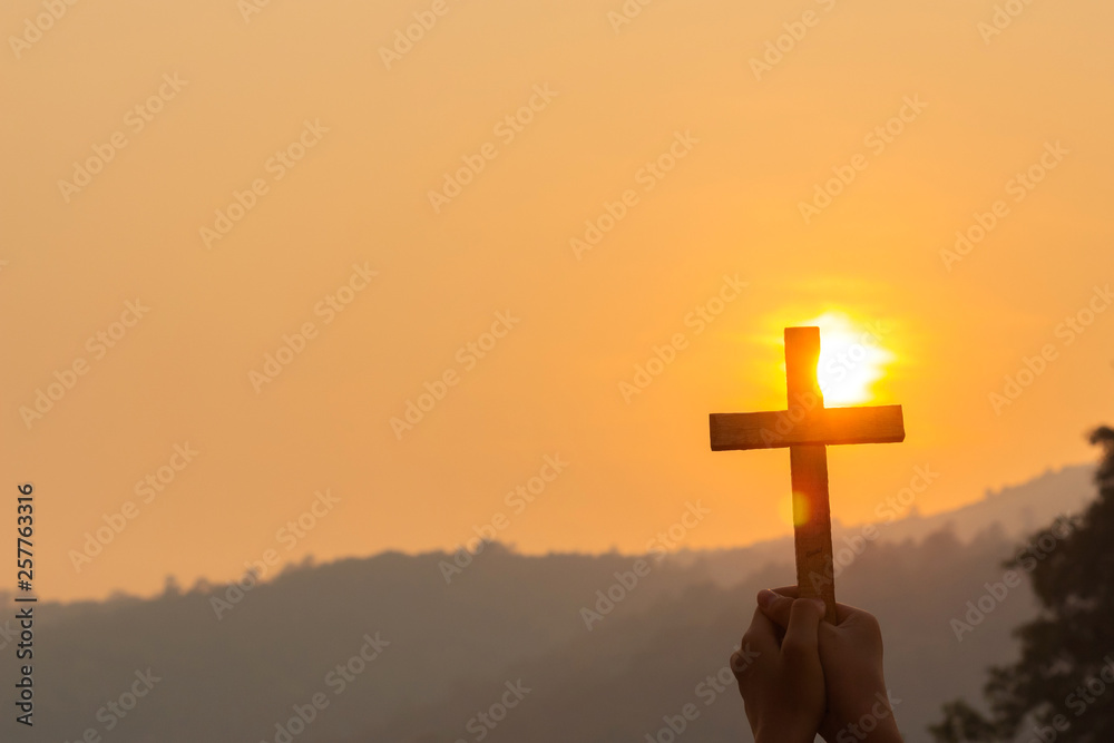 human praying to the GOD while holding a crucifix symbol at sunset