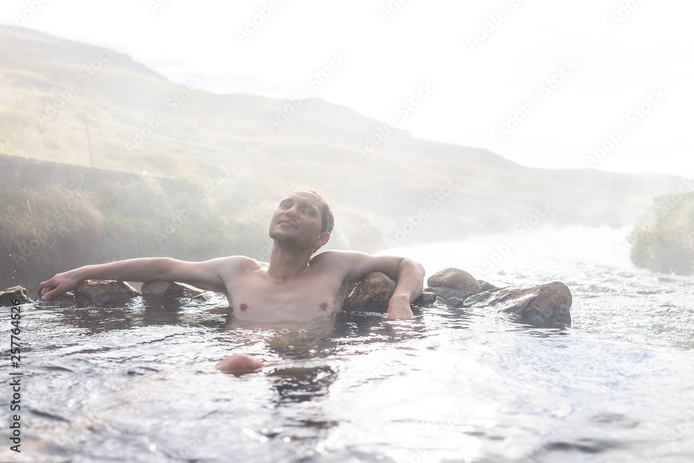 Young happy man swimming bathing relaxing in Hveragerdi Hot Springs in Reykjadalur during autumn morning day in south Iceland on golden circle rocks and river steam