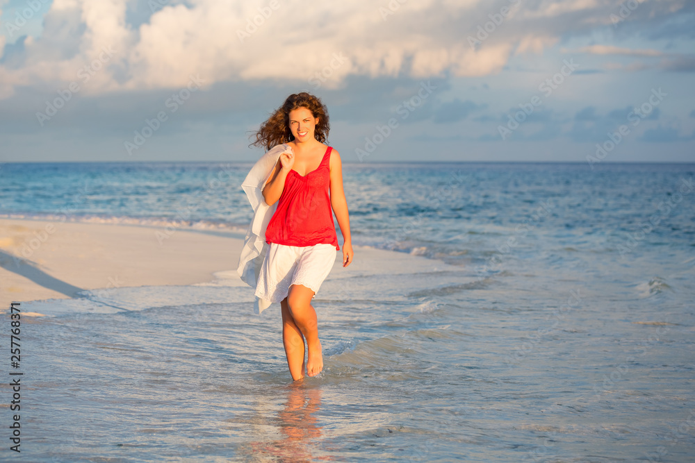 Attractive young woman walking along ocean beach in Maldives at summer vacation Attractive young woman walking along ocean beach in Maldives at summer vacation