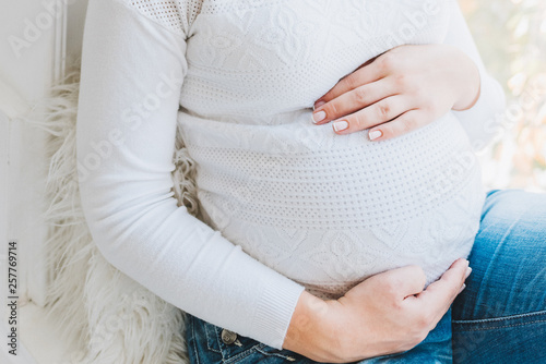 Beautiful caucasian pregnant woman wearing jeans and a white top. She is touching her belly. Pregnancy and expecting a baby.