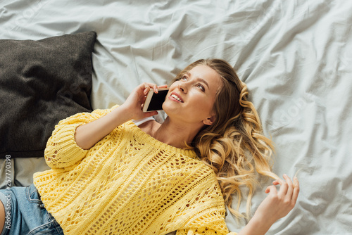 beautiful smiling girl lying in bed and talking on smartphone