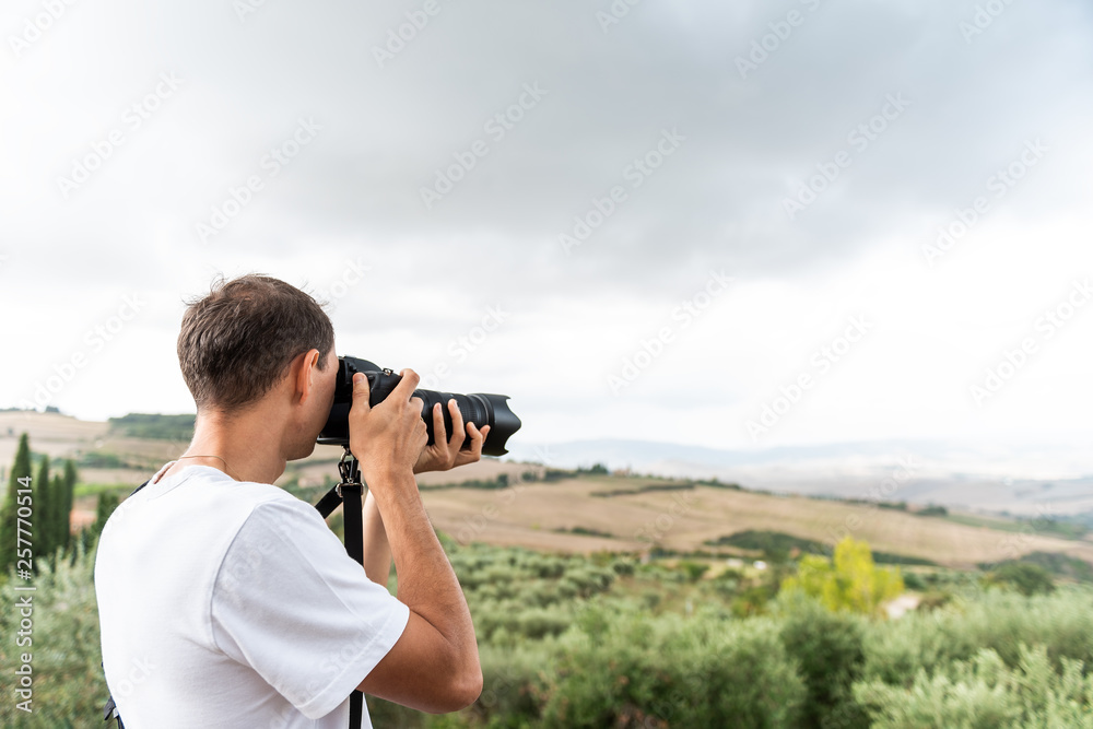 Val D'Orcia countryside in Tuscany, Italy with rolling green hills with farm landscape and young man tourist photographer taking picture with camera Val D'Orcia countryside in Tuscany, Italy with rolling green hills with farm landscape and young man tourist photographer taking picture with camera