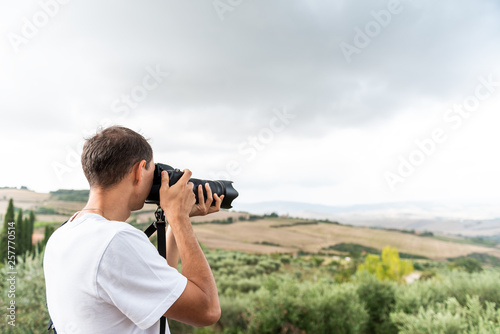 Val D'Orcia countryside in Tuscany, Italy with rolling green hills with farm landscape and young man tourist photographer taking picture with camera