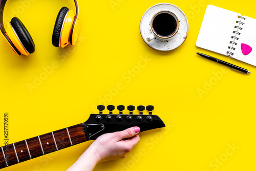 Musician work place with guitar, earphones, notebook and coffee on yellow background top view