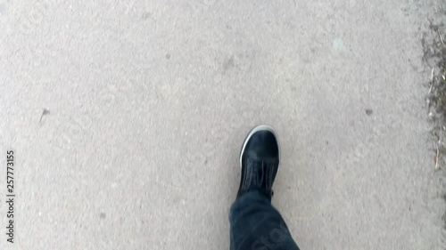 First person view of the feet of the guy who walks in sneakers on the asphalt.