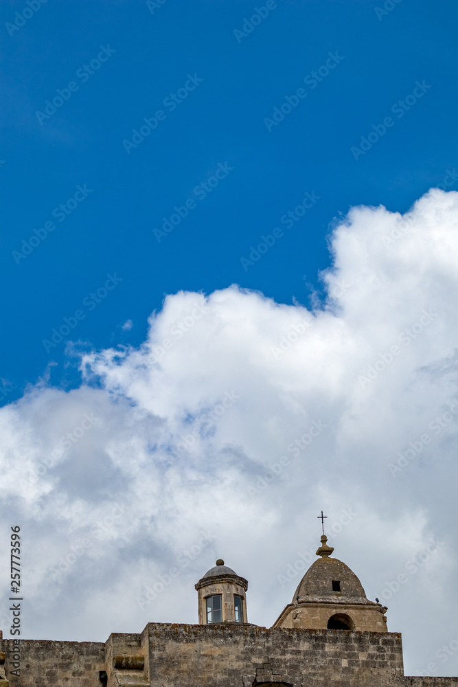 Obraz premium Summer blue sky and church roof with religious cross, view of ancient town of Matera, the Sassi di Matera, Basilicata, Southern Italy, cloudy summer August day