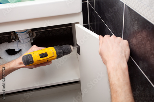 Wallpaper Mural Worker installing doors on the closet. Furniture repair and assembly concept. Young man assembling bathroom furniture. Hands close up.  Carpenter working with screwdriver. Torontodigital.ca