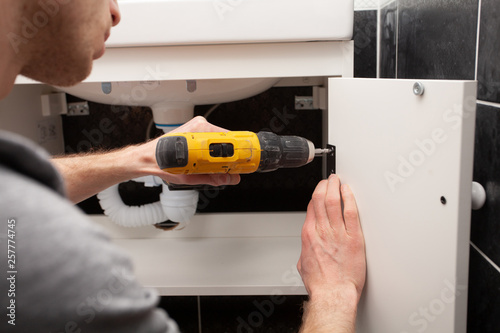 Worker installing doors on the closet. Furniture repair and assembly concept. Young man assembling bathroom furniture. Hands close up. Carpenter working with screwdriver.