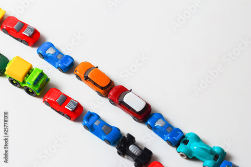 Plastic multi-colored toy cars are lined up on a white background. Stereotypical alignment of subjects is a sign of autism. Selective focus. Copy space for text. Traffic jams air pollution concept.
