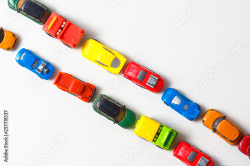 Plastic multi-colored toy cars are lined up on a white background. Stereotypical alignment of subjects is a sign of autism. Selective focus. Copy space for text. Traffic jams air pollution concept.