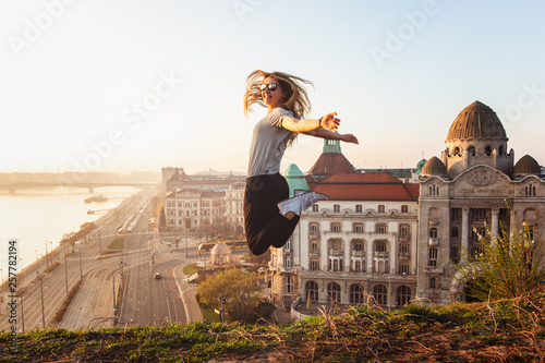 Beautiful woman jumping opposite famous facade and entrance to Hotel Gellert on banks of Danube in Budapest, Hungary photo