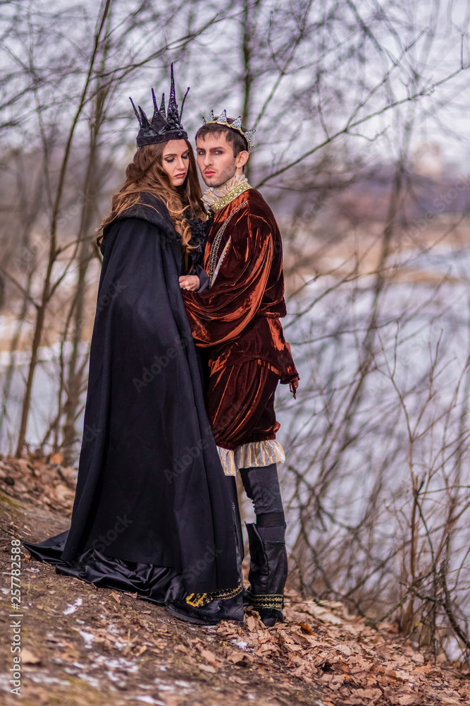 Caucasian Couple as King and Queen in Fur Medieval Outfit With Crowns Posing Together Outdoor. Caucasian Couple as King and Queen in Fur Medieval Outfit With Crowns Posing Together Outdoor.
