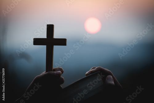 Billede på lærred close up young hands holding wooden cross over holy bible and praying