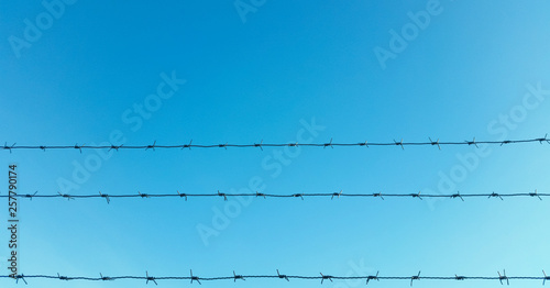 strands of barbed wire with blue sky and clouds in the background