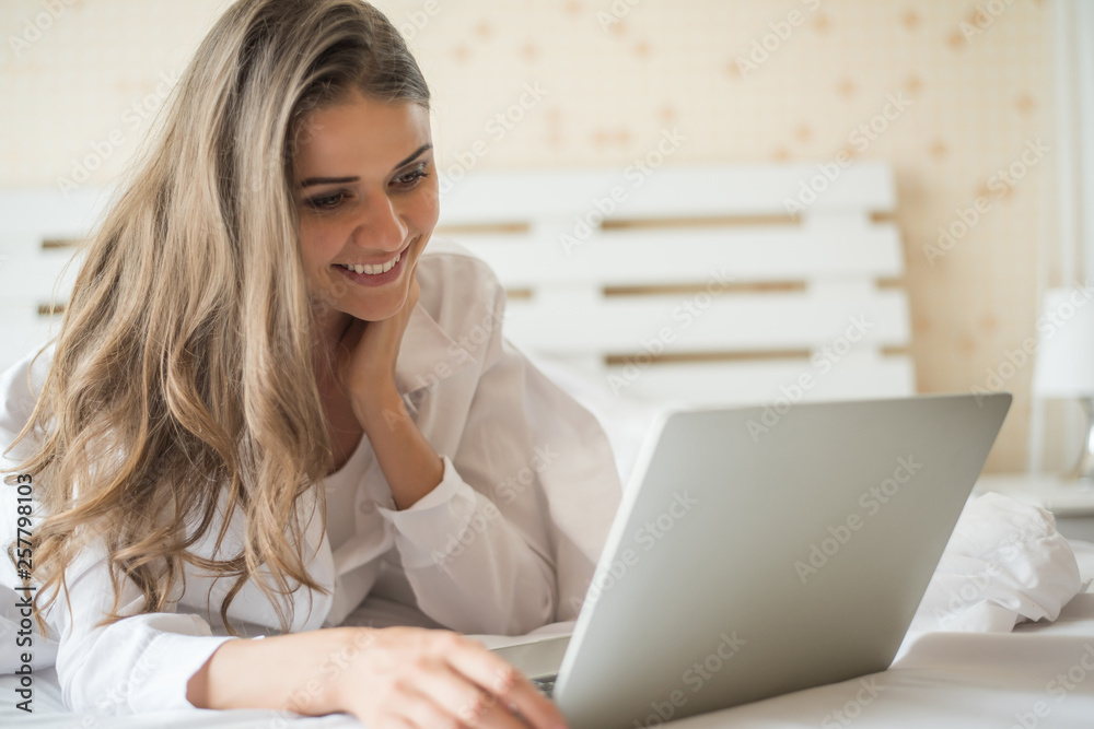 Happy Beautiful woman working on a laptop on the bed in the house Happy Beautiful woman working on a laptop on the bed in the house
