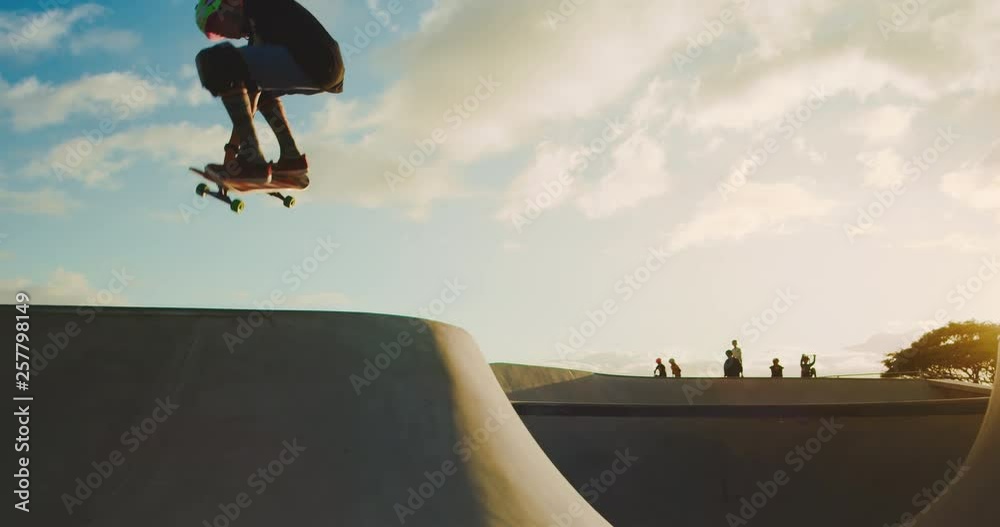 Skateboarder kid flying through the air in skate park at sunset, extreme skateboarding kid jumping high, young skateboarding shredder in slow motion