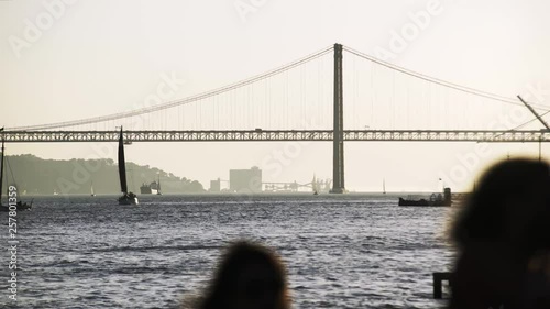 Embankment in Lisbon. View rio Tejo and unrecognizable traveler admiring beautiful view of majestic bridge 25th april on horizon photo