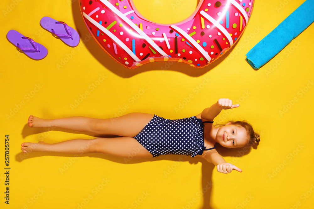 Φωτογραφία Top view of a little girl lying on the floor with slippers, a towel and an inflatable circle donut on the side