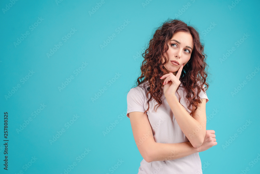 Attractive brunette girl with curly hair isolated over blue turquoise background thinking and making decision