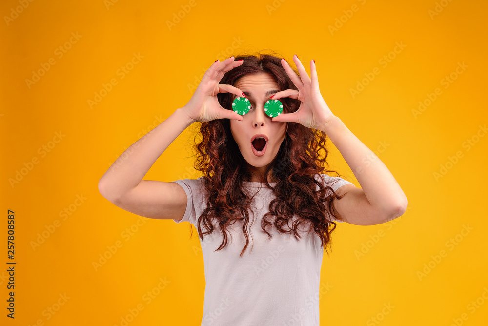 Attractive brunette girl with curly hair isolated over yellow background with poker chips in her hands. Online casino concept Attractive brunette girl with curly hair isolated over yellow background with poker chips in her hands. Online casino concept