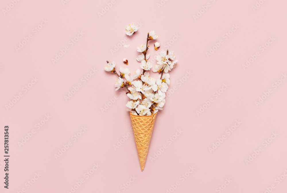 Fototapeta Waffle cone with bouquet of spring blooming branches of white flowers on pastel pink background. Creative spring minimal concept. Flat lay top view copy space.