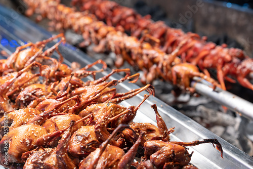 Rotisserie cooked Partridge covered with sesame seeds sold by a food hawker - BBQ spit roast Quail skewered over hot coals by Thai street food vendor in Thailand