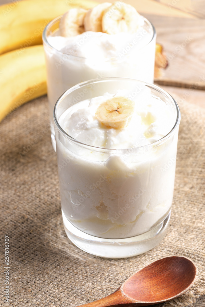 Two glasses of fat homemade yogurt with banana slices on burlap napkin. Two glasses of fat homemade yogurt with banana slices on burlap napkin.
