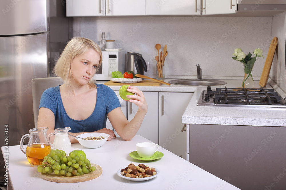 young woman eating healthy food in the kitchen at the table. disappointment in healthy eating tired to eat right, tired of dieting. young woman eating healthy food in the kitchen at the table. 