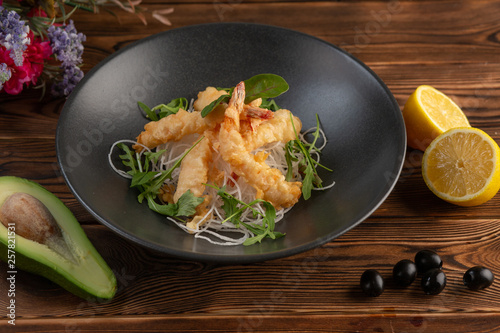 Tempura shrimps with tartar sauce on a black plate on a wooden background