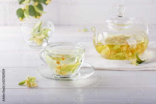 Linden tea in a transparent tea pot. Glass cup and tea pot with herbal lime tree tea on white background. Medicinal plant, flowers used for herbal teas and tinctures.