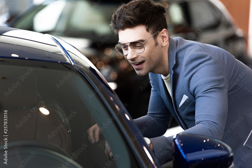 happy customer in glasses standing near automobile in car showroom ac