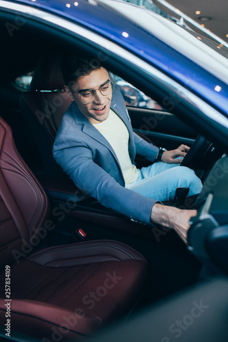 selective focus of successful cheerful man in glasses sitting in automobile