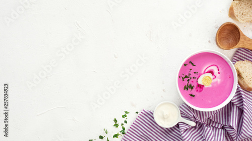 Soup with beets, eggs and greens on white background with bread, sour cream and wooden spoon. Beetroot soup. Eye bird view. Copy space.