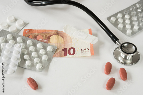 Assorted pharmaceutical medicine pills, tablets, stethoscope and money against white background photo