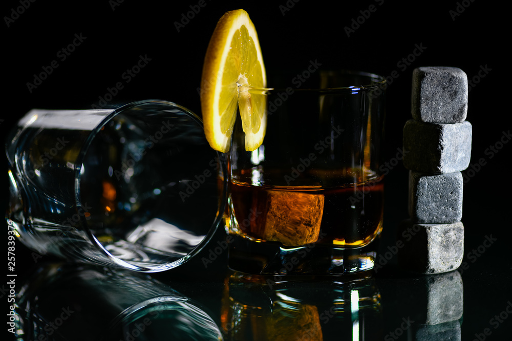 glasses of whiskey on a glass table with a lemon isolated on a black background, special stones for whiskey. glass objects