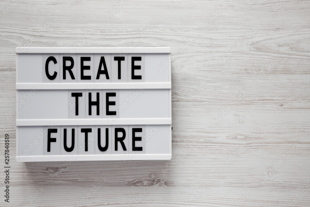 'Create the future' words on lightbox on a white wooden surface, top view. From above, flat lay, overhead. Space for text.