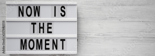 'Now is the moment' words on modern board on a white wooden background, top view. From above, flat lay, overhead. Copy space.