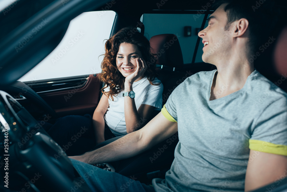 cheerful curly woman sitting in automobile with happy handsome man